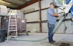 Trent Cook empties treated waste into the Maximizer, the machine on the left that looks somewhat like a trash bin on wheels, that separates solid from liquid waste. The waste is then sprayed onto nearby hay fields as fertilizer. –photo by Mitch Green/Telegram