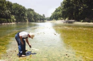 Brad Ware, who owns 2 miles of riverfront on his property in Killeen, stands in the Lampasas River as he picks up some algae that has formed.